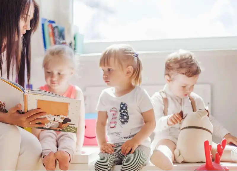 Une professionnelle lit une histoire à trois enfants dans la crèche